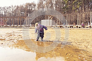 child in a hat and overalls enters a large dirty pool