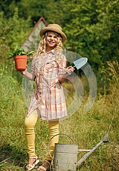 Child in hat with shoulder blade small shovel hoe. Happy smiling gardener girl. Little kid hold flower pot. Spring