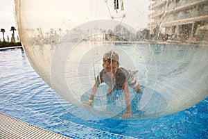 Little boy have fun inside big plastic balloon on the water of swimming pool on the summer resort. Kid inside big inflatable