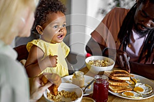 Child having breakfast. Kid eating poridge. Little girl at dining table with parents in kitchen