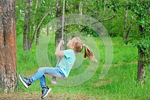 Child having  fun outdoors swinging on wooden homemade swing tied to a tree with a rope in spring or autumn