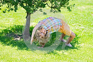 Child having fun at park outdoor. Happy kid boy standing upside down on green grass. Healthy lifestyles concept. Summer