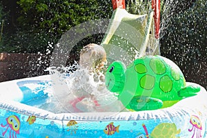 Child having fun playing in water in a garden paddling pool the boy is happy and smiling