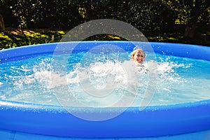 A child is having fun in a rubber pool. A girl splashes in an inflatable pool in the garden on a sunny summer day