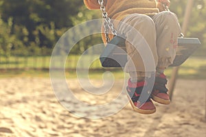 Child having fun with swing on a playground in bright afternoon sun - legs angled