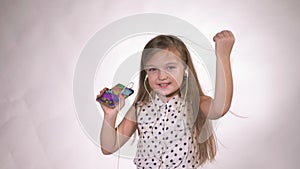 Child with headphones dancing at studio background. Girl listens to music on smartphone. Beautiful cute happy little