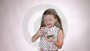 Child with headphones dancing at studio background. Girl listens to music on smartphone. Beautiful cute happy little