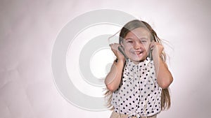 Child with headphones dancing at studio background. Girl listens to music on smartphone. Beautiful cute happy little