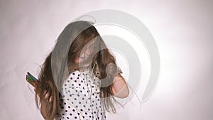 Child with headphones dancing at studio background. Girl listens to music on smartphone. Beautiful cute happy little