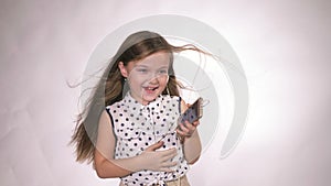 Child with headphones dancing at studio background. Girl listens to music on smartphone. Beautiful cute happy little