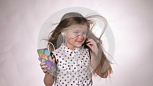 Child with headphones dancing at studio background. Girl listens to music on smartphone. Beautiful cute happy little