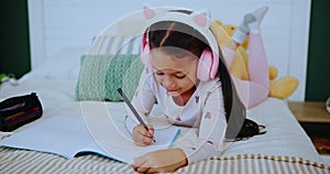 Child, headphones and girl with book in home, music and drawing or writing on bed for childhood development. Growth