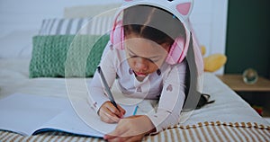 Child, headphones and girl with book in house, music and drawing or writing on bed for childhood development. Growth