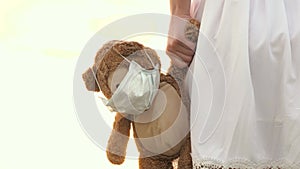 child health concept. child holds his beloved teddy bear in a protective mask during quarantine. girl carries in her