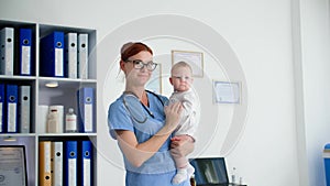 child health, female pediatrician in glasses with a small child in her arms while receiving patients stands in medical