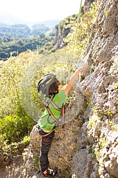The child in helmet is climbing on a natural terrain