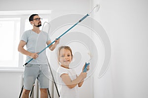 The child helps her father, who is standing behind her, near the wall, in the repair.