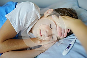 Child with high temperature lying in bed with closed eyes. Termometer lying near Child. Medical background photo