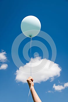 A child is holding a balloon on a string. Air balloon on the background of the sky. Rise to the sky. Light, weightless. Holiday photo