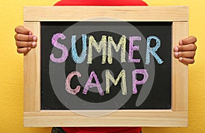 Child holding blackboard with words SUMMER CAMP