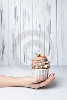 Child holding chocolate cupcake with cream cheese frosting, strawberry and blueberry on light background