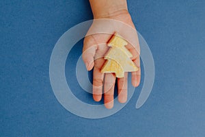 child holding a Christmas tree cookie in hand, blue paper background