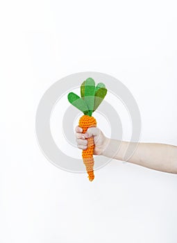 The child is holding a knitted carrot in his hand. Easter rabbit. Child`s hand.