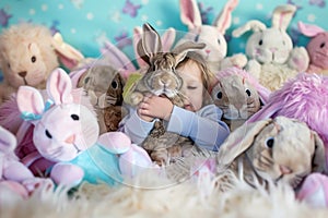 child holding a live rabbit among bunny plushies