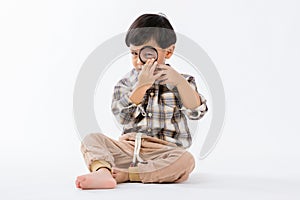 Child holding magnifying glass on white background. Boy with a magnifying glass in studio.