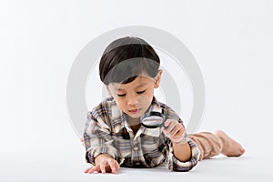 Child holding magnifying glass on white background. Boy with a magnifying glass in studio.