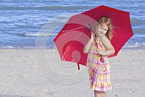 Child holding a red umbrella at beach