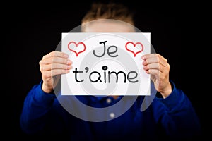 Child holding sign with French word Je T aime - I Love You