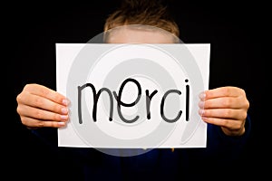 Child holding sign with French word Merci - Thank You