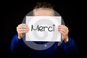 Child holding sign with French word Merci - Thank You