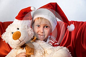 Child holding teddy bear. Kid dressed in Santa Claus hat. Baby playing at home. Christmas gift. Xmas holiday concept