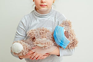 Child is holding toy bear in medical mask
