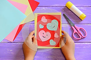 Child is holding a Valentines day card in his hands. Small child made a Valentines day greeting card. Cute and simple paper crafts