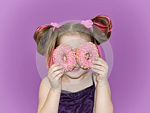 Child holds donuts near his eyes and looks through the holes like through glasses.