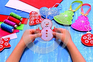 Child holds a felt snowman ornament in his hands. Christmas sewing crafts concept. Christmas tree, heart, star, snowman crafts