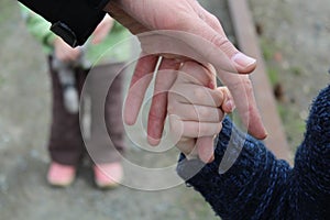 The child holds the finger of the father`s hand against the background of another child`s brother or sister