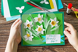 The child holds Mother`s Day card with daffodils. Handmade.