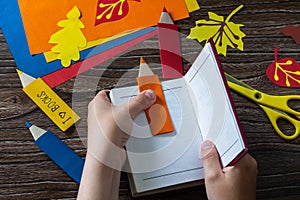 Child holds multi-colored bookmarks origami pencil made of paper new school year on a wooden table.