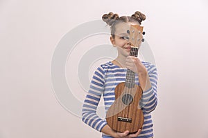 A child holds a ukulele in his hands. Small creative children. Girl learns to play an instrument online