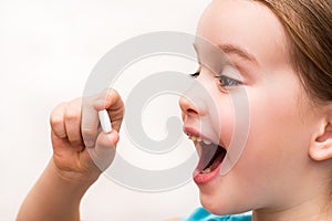 The child holds a white oval tablet in his hand and wants to swallow it with joy. Medicines and synthetic vitamins