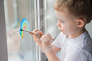 Child at home draws a rainbow on the window photo