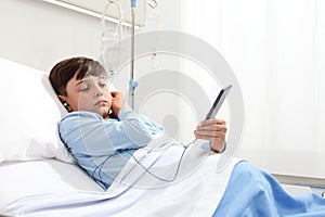 Child in hospital bed using smartphone surfs the internet wearing earphones photo