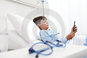 Child in hospital bed using smartphone surfs the internet wearing earphones photo