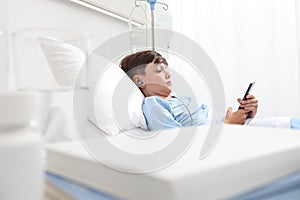 Child in hospital bed using smartphone surfs the internet wearing earphones photo