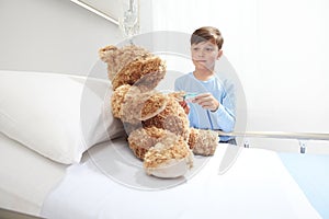 Child in hospital room playing with a pulse oximeter and a teddy bear imitating doctor