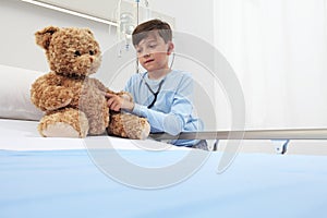 Child in hospital room playing with a stethoscope and a teddy bear imitating doctor photo